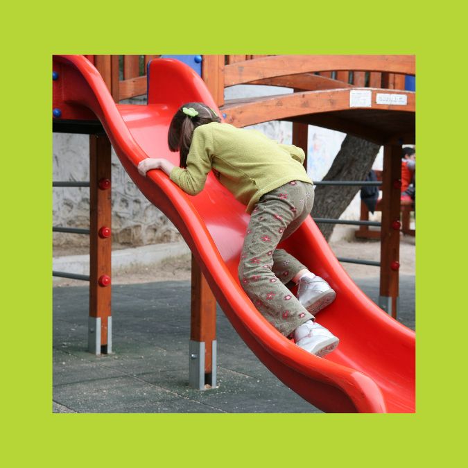 Girl climbing backwards up playground slide